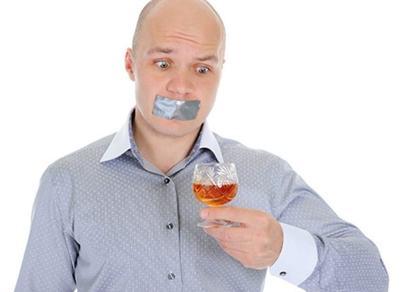Мужчина держит бокал спиртного с закрытым ртом
